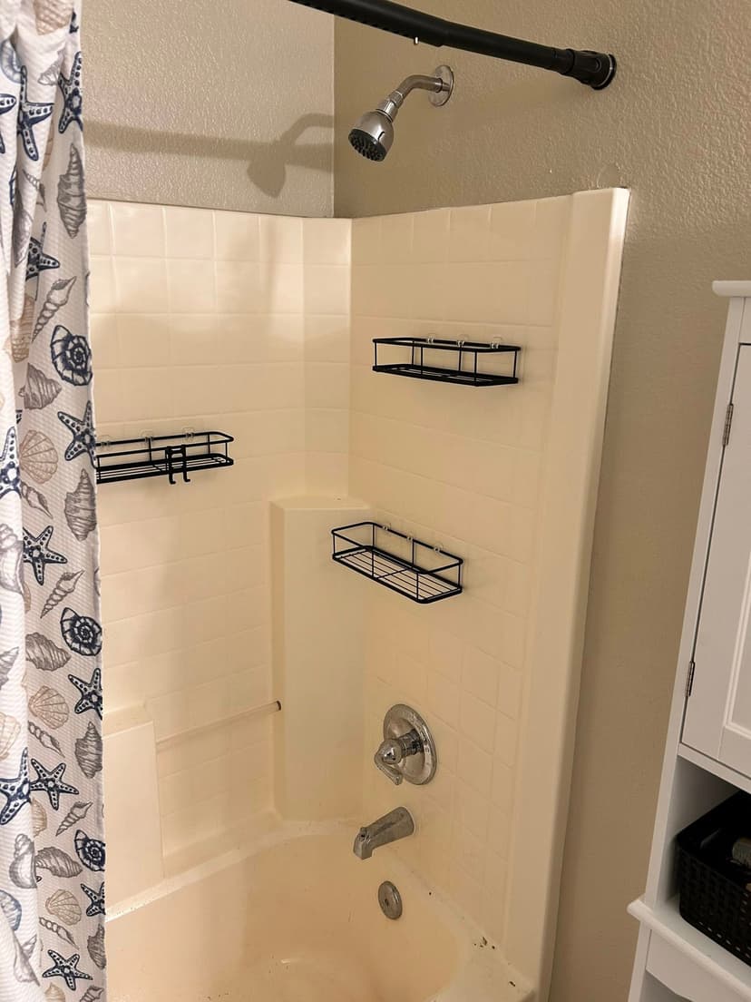 Modern bathroom shower with decorative curtain and black storage shelves on tiled walls.