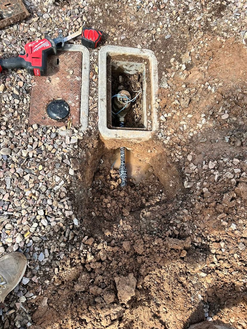 Excavated area showing a concrete box, plumbing equipment, and soil around it.